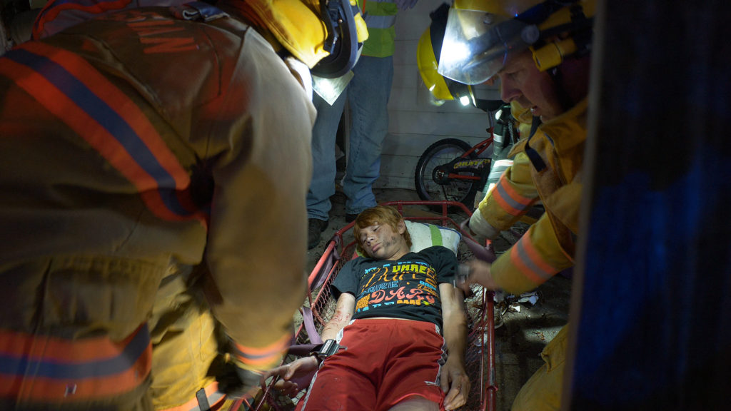 First responders equipped with headlamps, load a young patient onto a gurney
