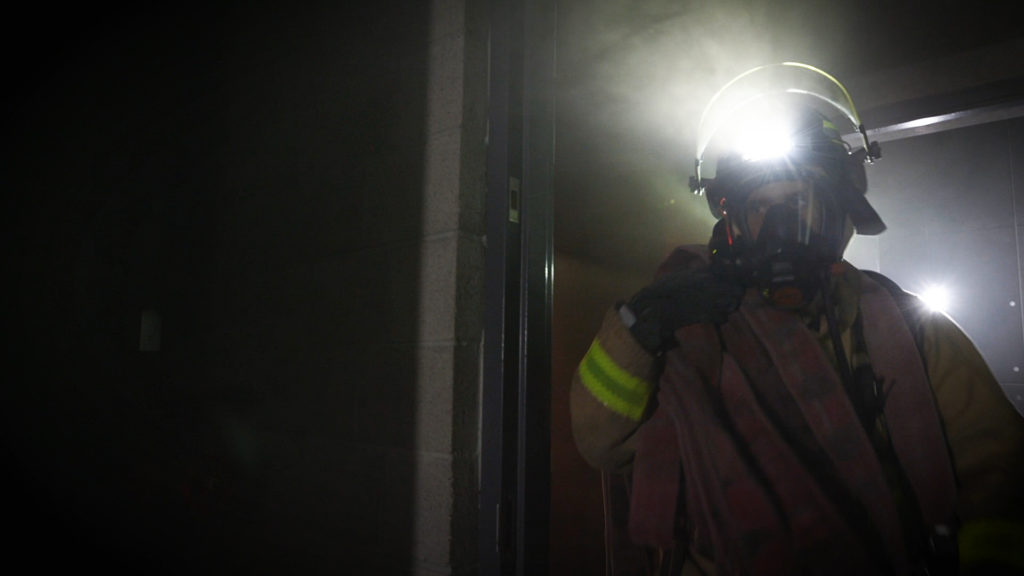 Firefighter equipped with a FoxFury Discover helmet light enters a structure 